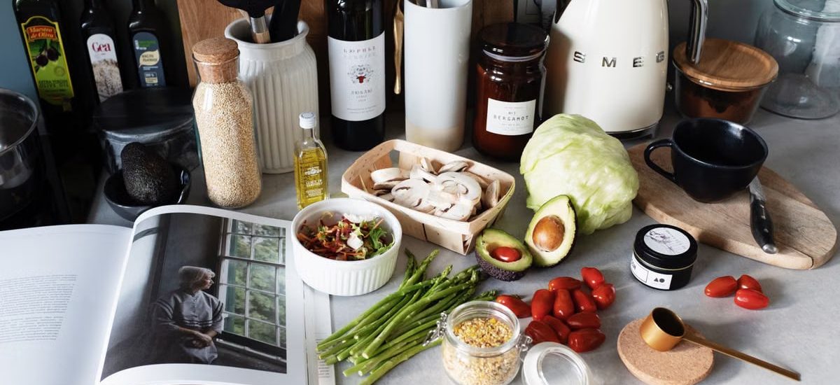 Various colorful healthy food and vegetables locating on countertop next to many different utensils and white kettle during cooking in stylish kitchen