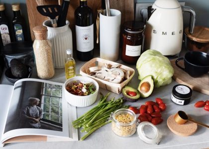 Various colorful healthy food and vegetables locating on countertop next to many different utensils and white kettle during cooking in stylish kitchen